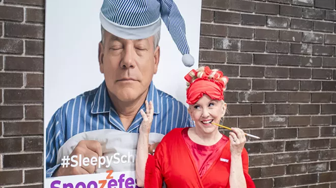 a woman stands by a poster of a sleeping david schweikert