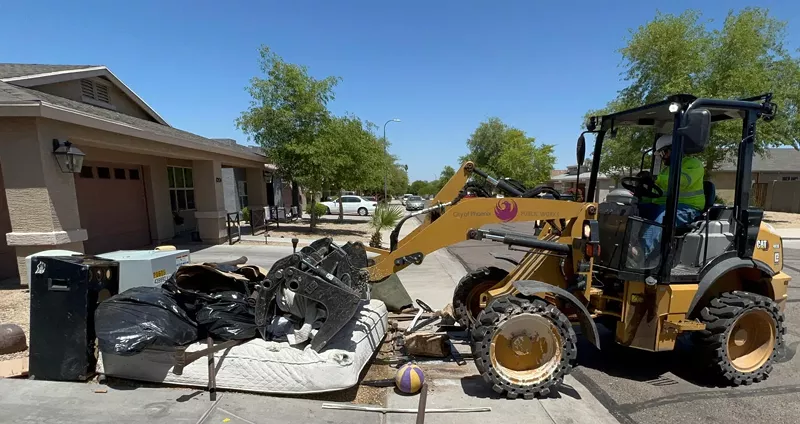 Image: A City of Phoenix backhoe loader scoops up debris on a residential curb.