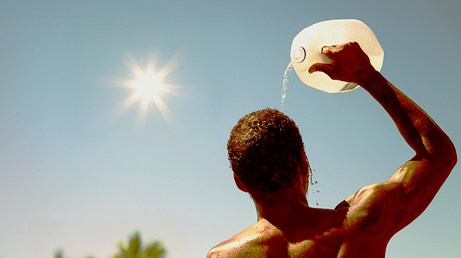 A man under a glaring sun pours water over his head out of a jug.