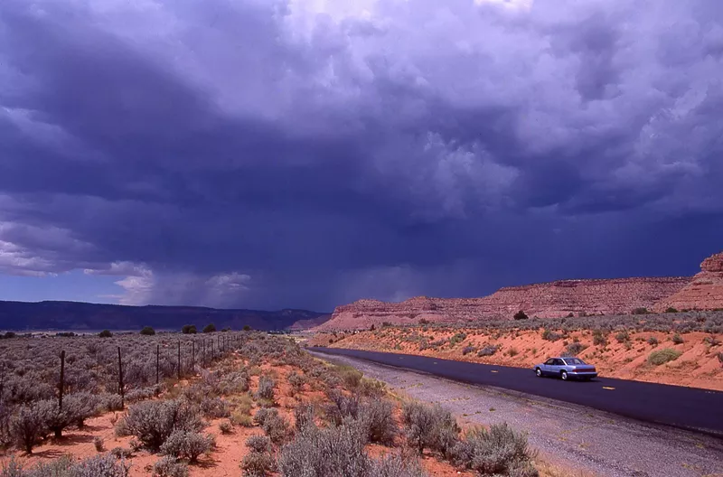 Image: a rural southwestern road with gray clouds above