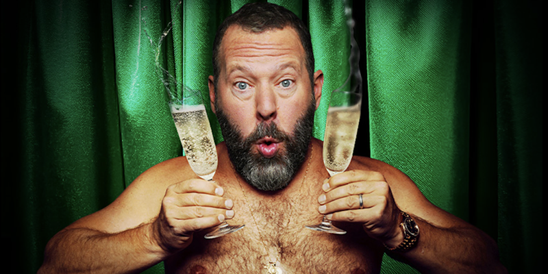 Image: A shirtless man holding glasses of Champagne.