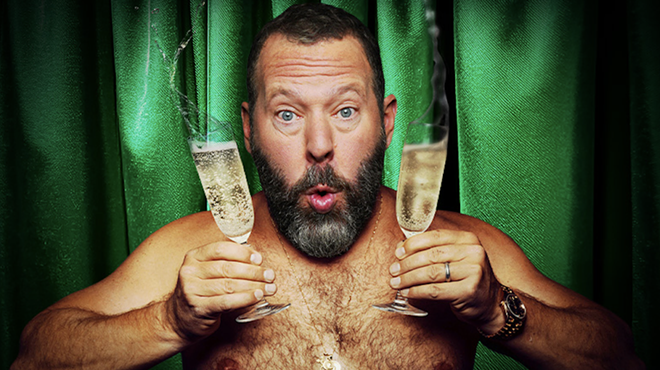 A shirtless man holding glasses of Champagne.