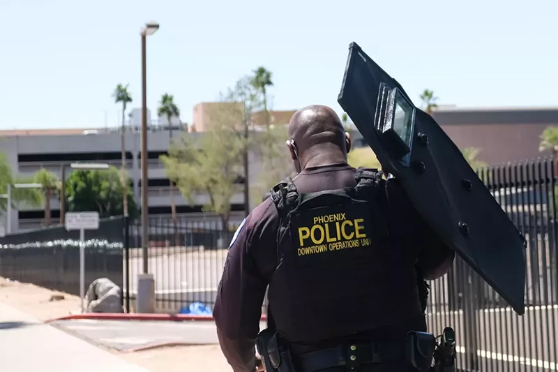 Image: a phoenix police officer, seen from behind, holding a riot shield
