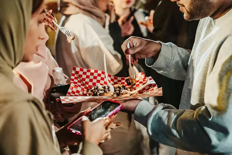 Image: People share a plate of food at a festival.