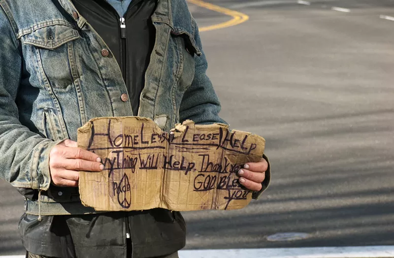Image: a man holding a cardboard sign near a road
