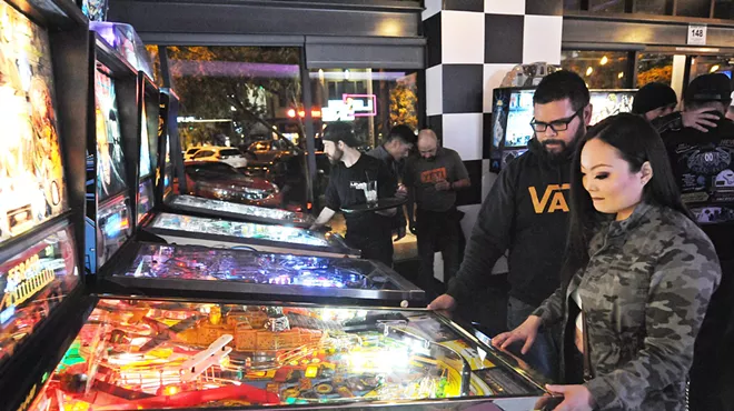 People playing pinball in an arcade.