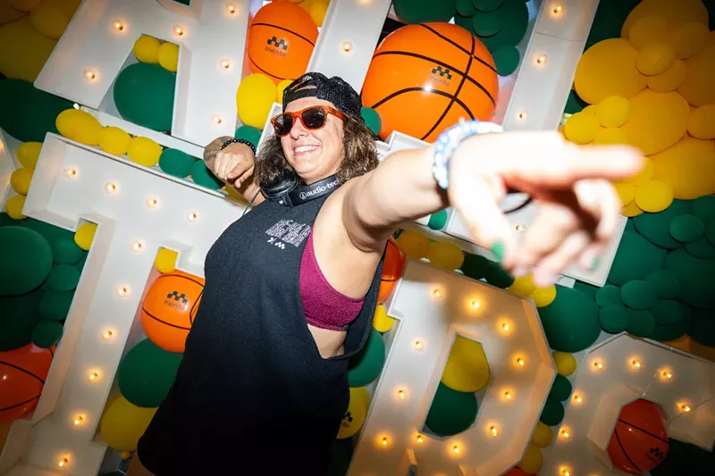 Image: a woman points at the camera in front of an "All Stars" sign with balloons