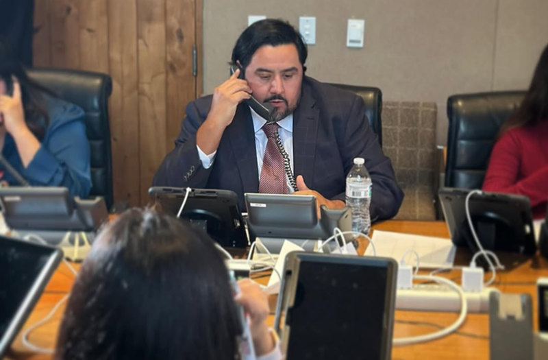 Image: a man at a conference table speaks on the phone
