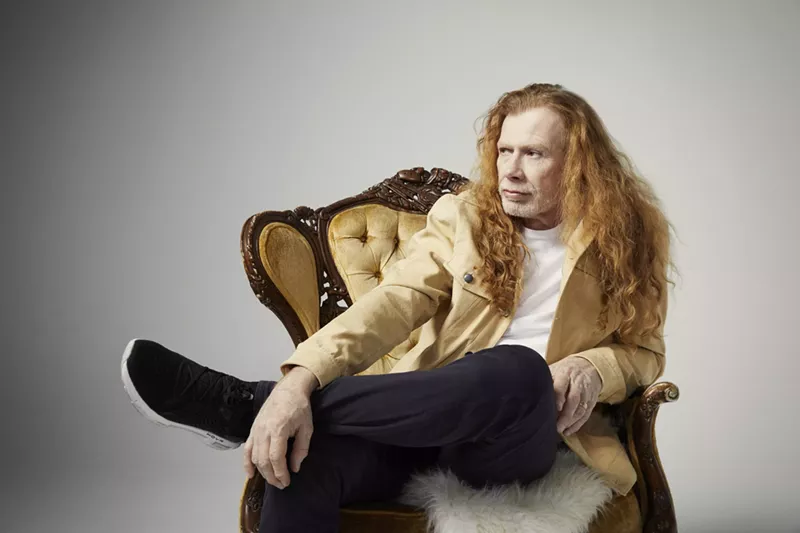 Image: An older man with long hair posing for a photo in a chair.