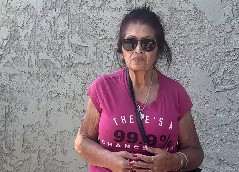 Image: An older woman in sunglasses against a stucco wall