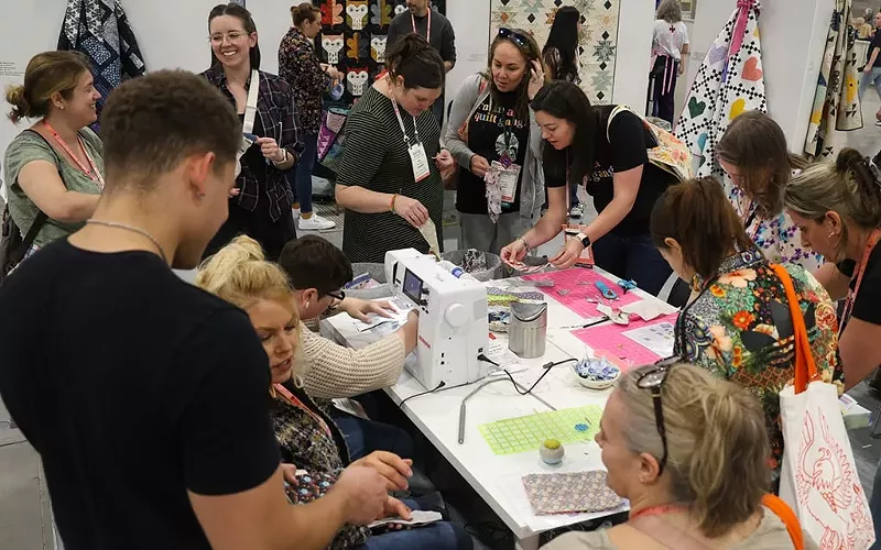 Image: Attendees of QuiltCon practice sewing fabric at a booth hosted by Cotton+Steel Fabrics.