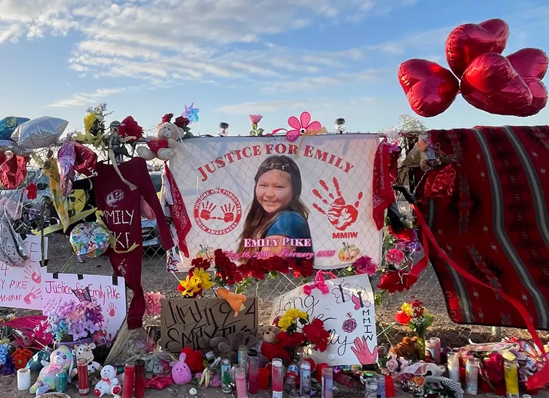 Image: a memorial with candles and balloons and flowers and a picture of a teenage Native American girl