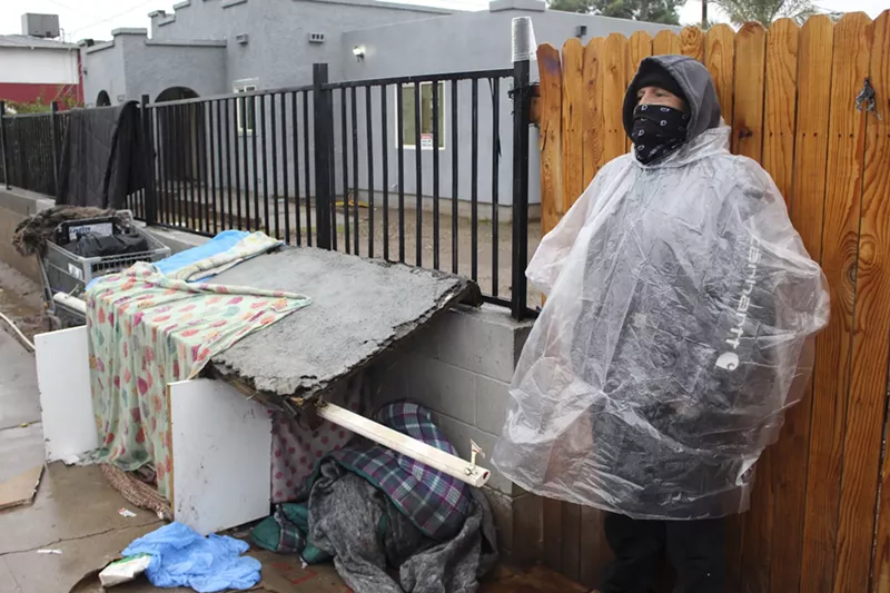 Image: A man in a rain poncho stands on a street.