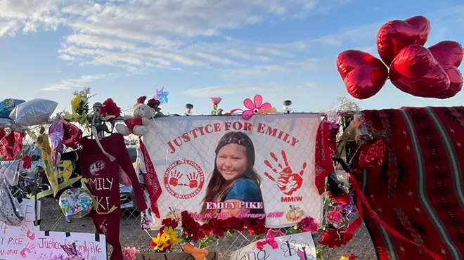 a memorial with candles and balloons and flowers and a picture of a teenage Native American girl