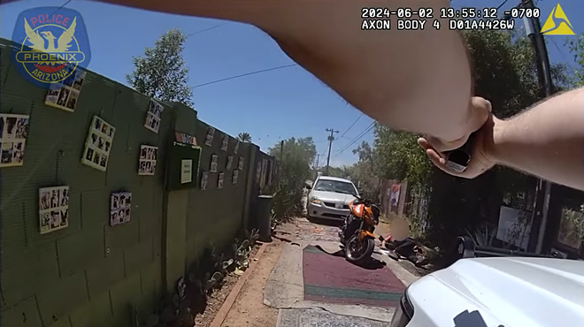 Body-cam footage showing two arms holding a gun on a blurred-out person who is laying on the ground next to a motorcycle.
