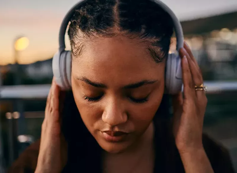 Image: Close-up of a serene young woman with braided hair and headphones, enjoying music during sunset outdoors, creating a peaceful moment.