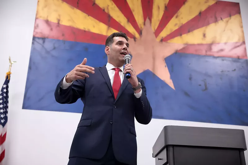 Image: rodney glassman speaks in front of an arizona flag background