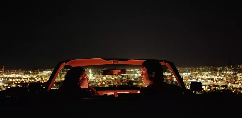 Image: A couple in a convertible overlooking a city.