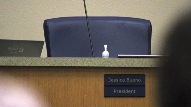 an empty chair at a public meeting with a "jessica bueno" placard