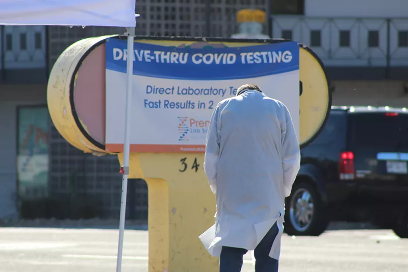 Image: Premier Lab Solutions has a clinic along 16th Street in Phoenix. A worker takes a quick break between administering COVID-19 tests to patients in a long line of cars.