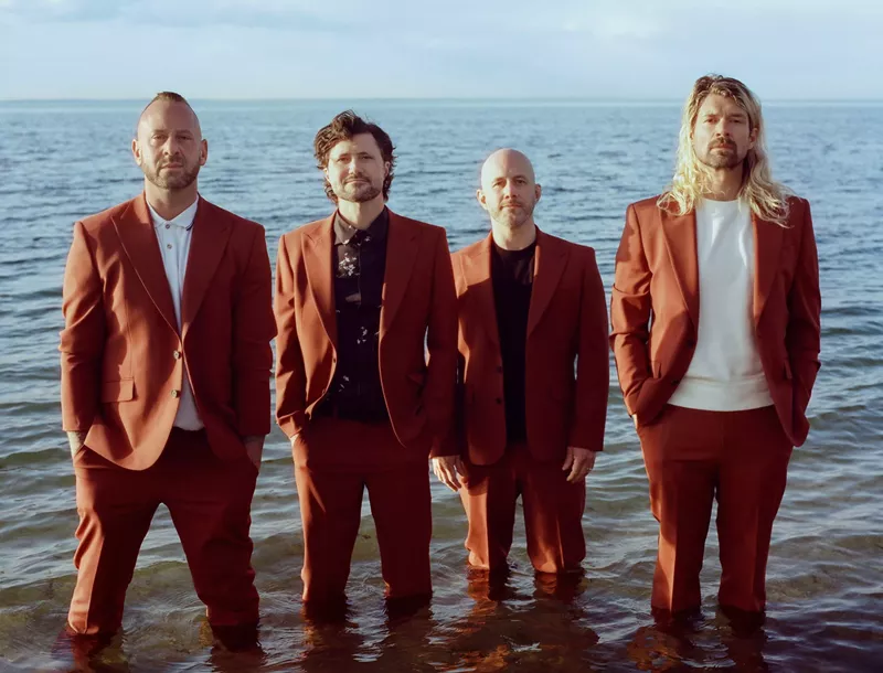 Image: Four men in suits standing in the water.