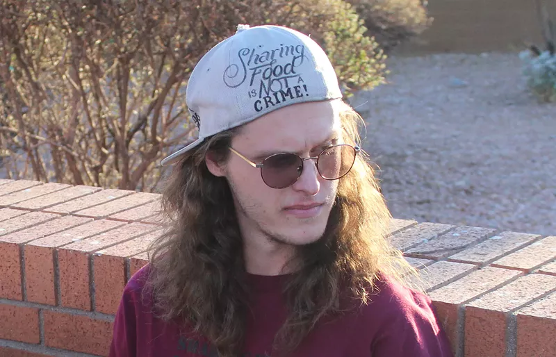 Image: a young man in a backward hat that says "sharing food is not a crime"