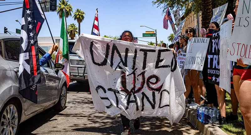 Image: a woman walks down the street holding a banner that says "united we stand"