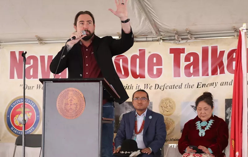 Image: eli crane speaks at a podium in front of a "navajo code talkers day" banner