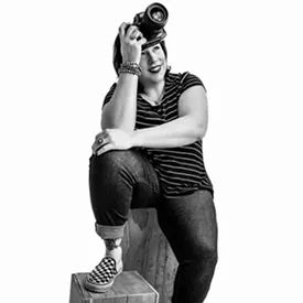 Black and white picture of a woman smiling with her foot propped up on a chair and her head resting in her hand.