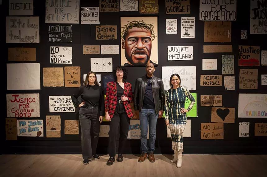 Four people stand in front of a wall covered in signs.
