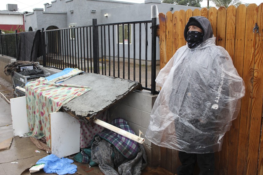 A man in a rain poncho stands on a street.