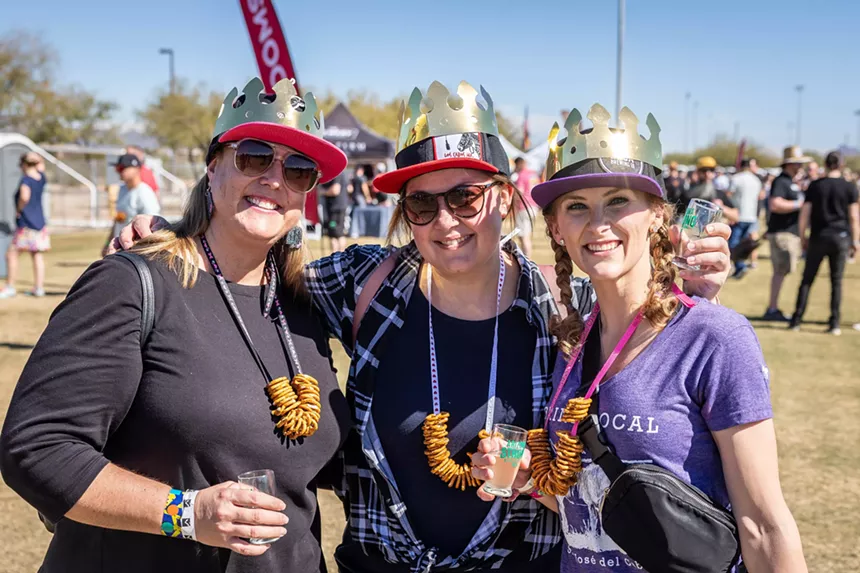Three women at a beer festival with pretzels and crowns.