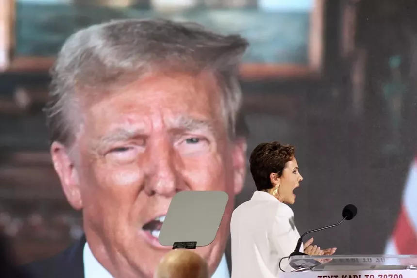 Kari Lake on stage, a huge image of Donald Trump behind her