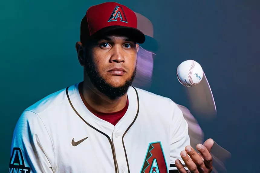 A baseball player sits while idly tossing a ball in the air.