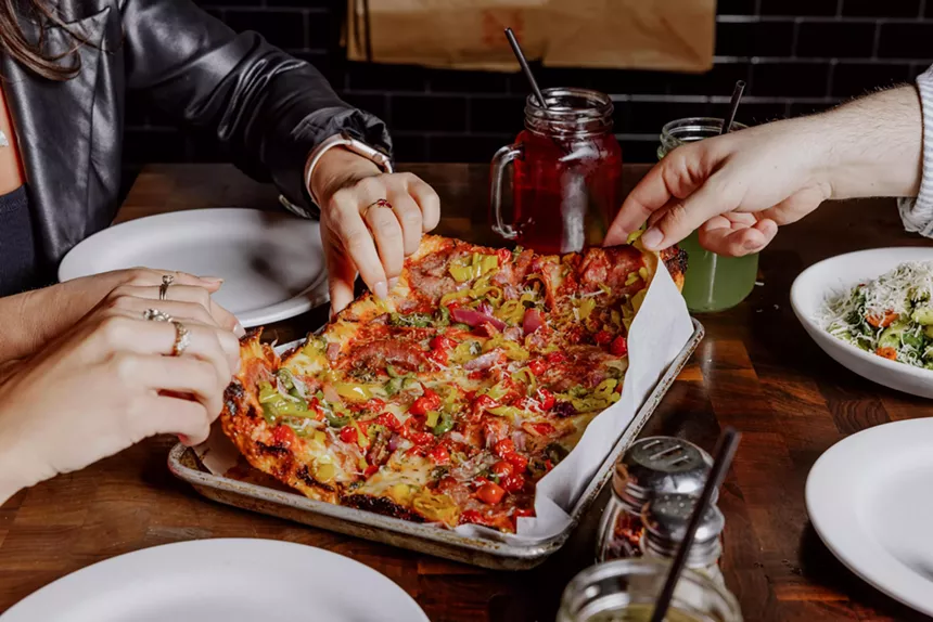 Grabbing slices of a Detroit-style pan pizza.