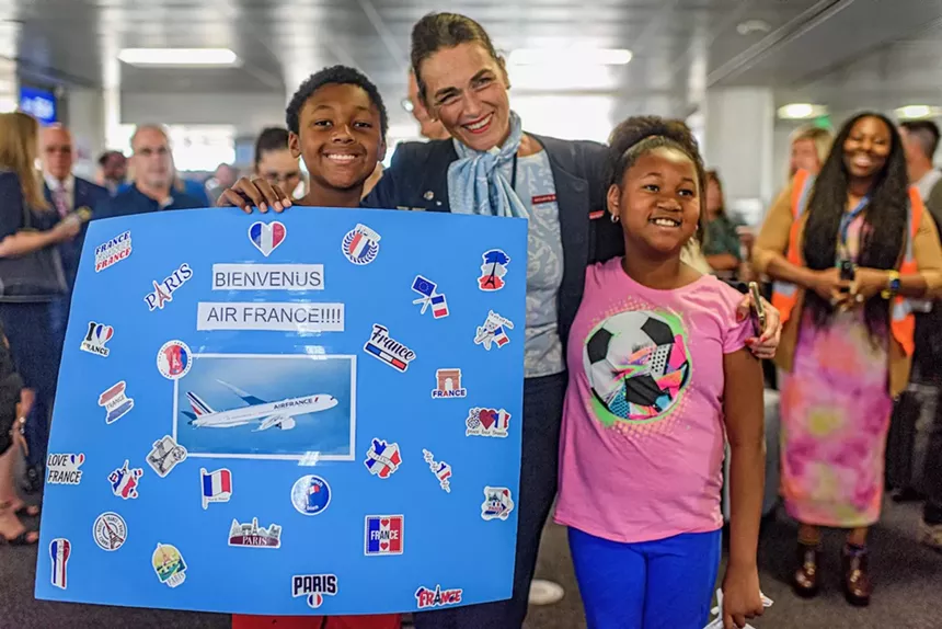 Two children pose holding a sign pose with a flight attendant