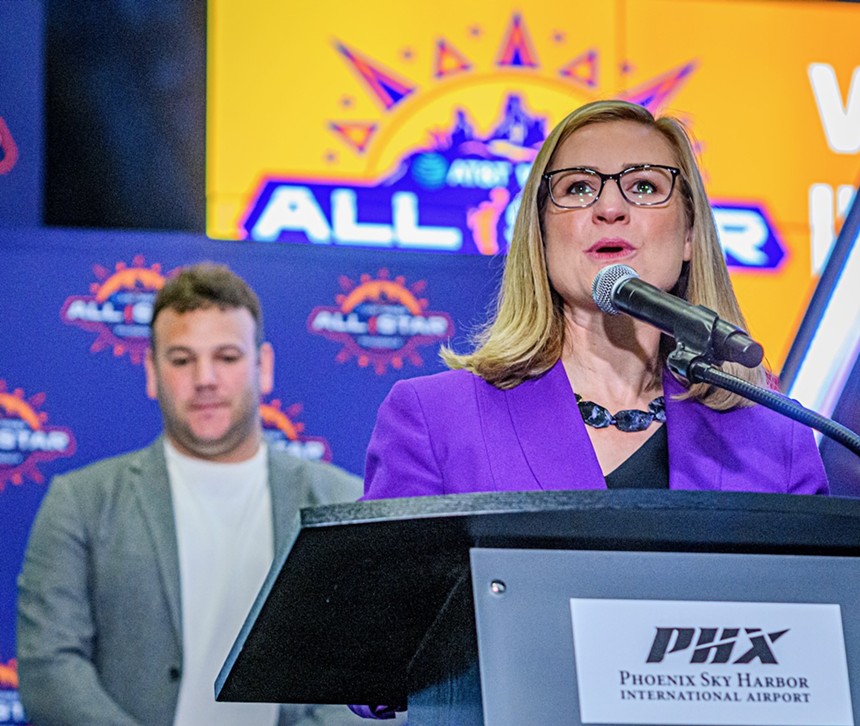 A woman in a purple blazer speaks at a podium
