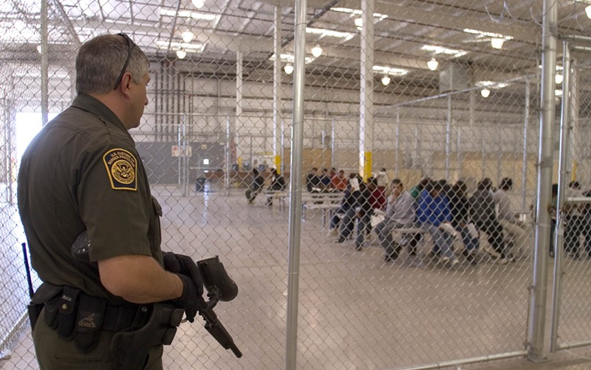An armed immigration officer looks at migrants in a holding pen.
