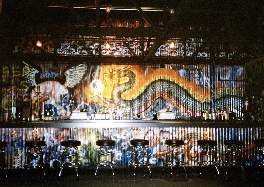 A bar with the background of a colorful mural of a dragon.