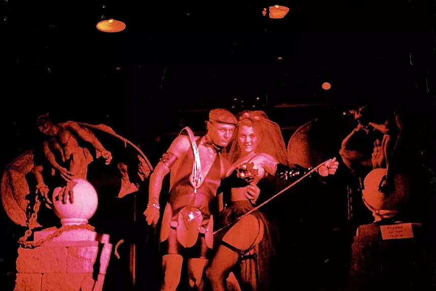 Two costumed nightclub patrons standing between two statues.
