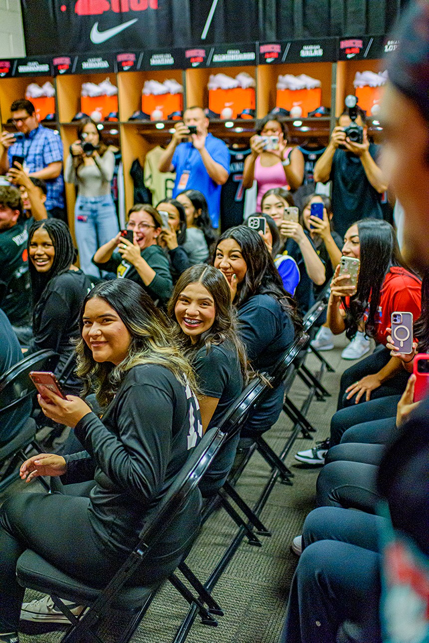 A crowd of seated high school girls look toward the camera in surprise
