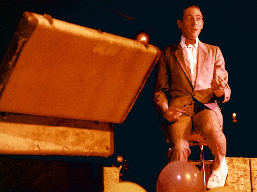 A comedian onstage with a suitcase.