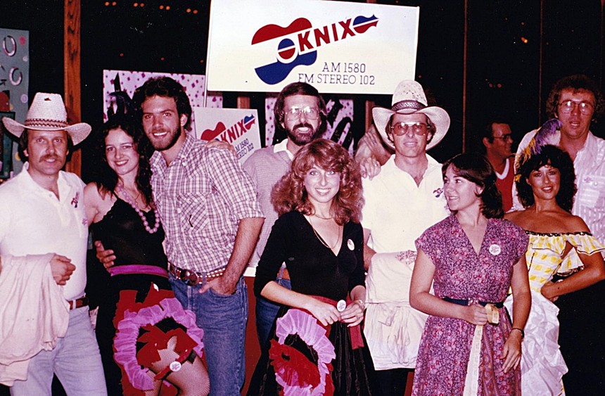 A group of men and women in western wear standing in front of a radio station sign.
