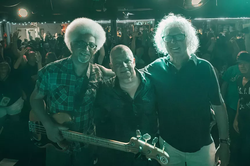 Three men posing on a stage with the crowd behind them.