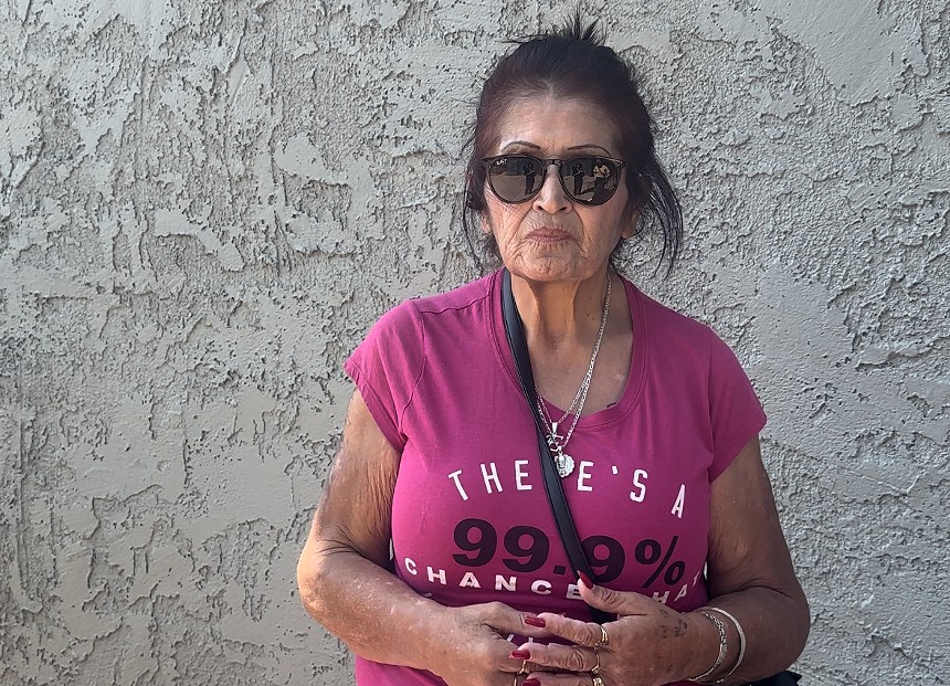 An older woman in sunglasses against a stucco wall