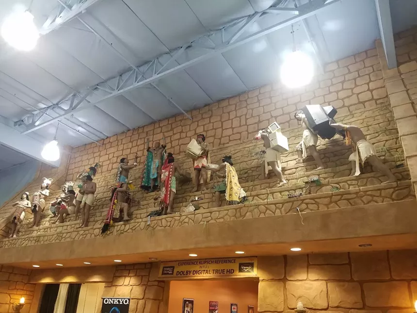 A store display of mannequins that look like ancient Aztecs carrying pieces of modern technology.