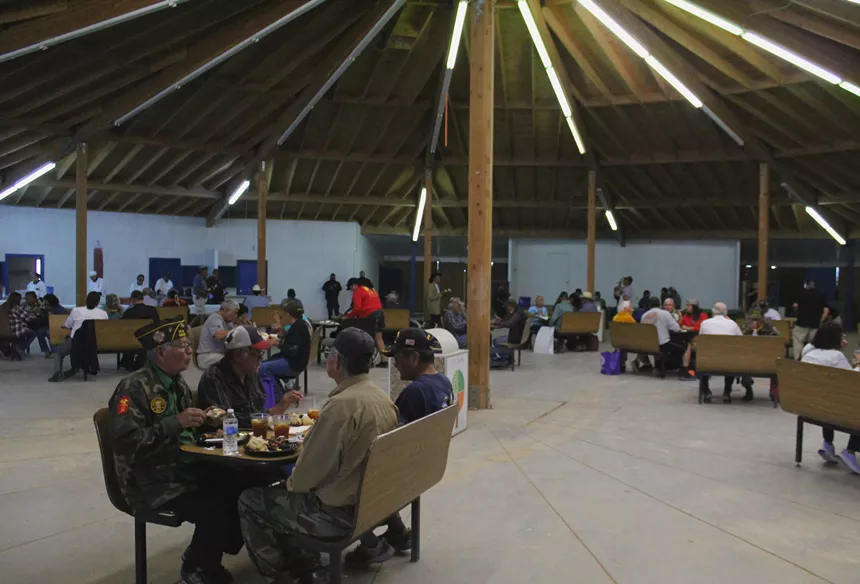 People sit at tables in a large, rounded wood room with a high ceiling.