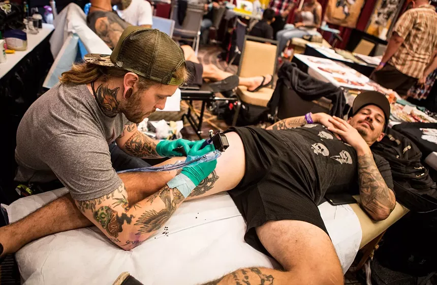 A man gets a leg tattoo while lying on a table.