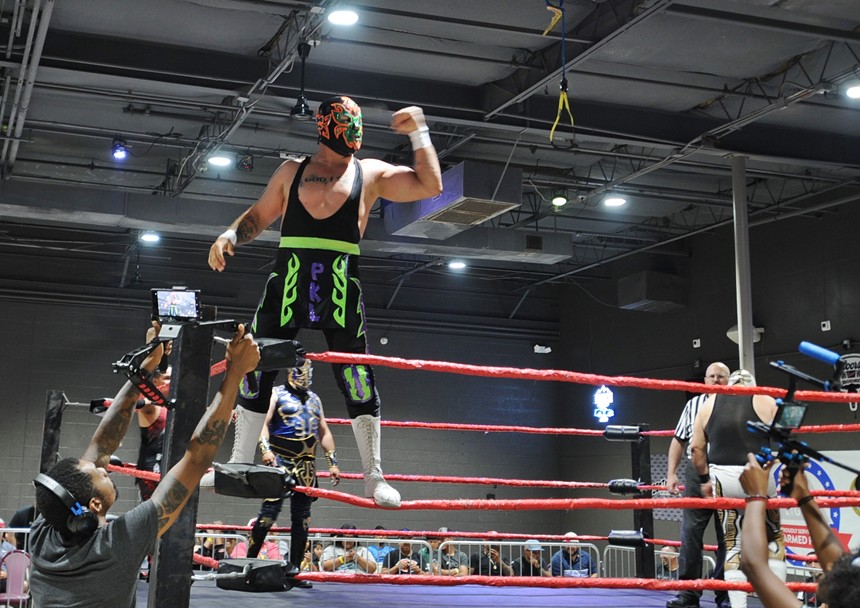 A masked wrestler stands on the turnbuckle of a wrestling ring.