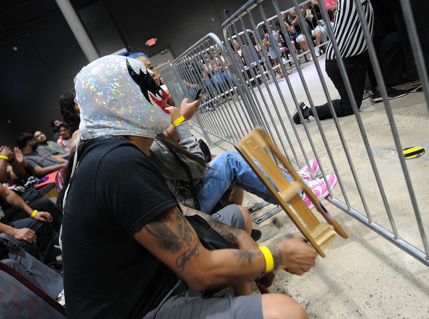 A masked wrestling fan sits at ringside.